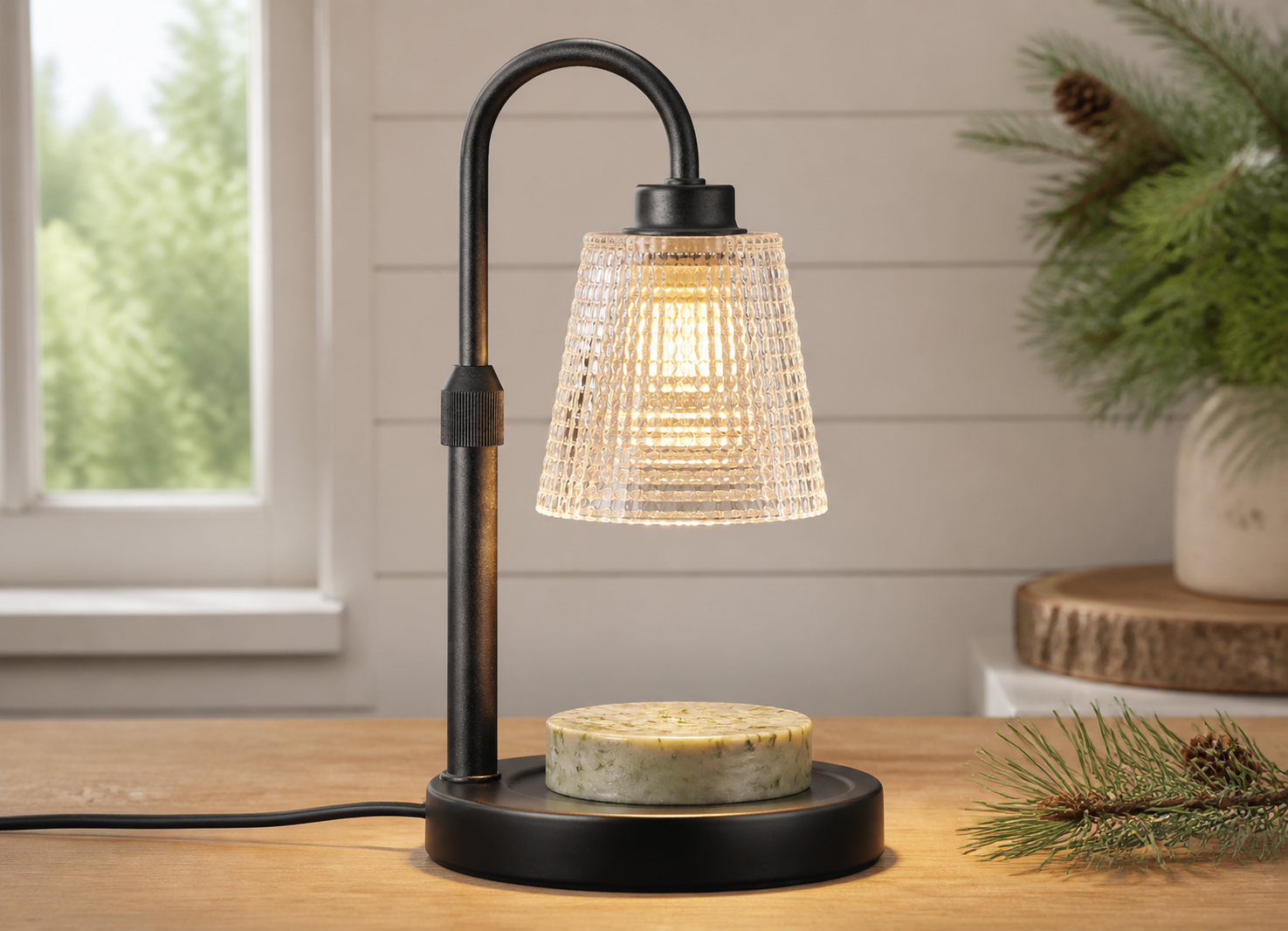 Head-on view of a corded glass-shade warming lamp with a flat pale green pine-wax disk on a wood table.